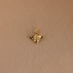The Honeybee Charm in 18K Gold, adorned with small gemstones, is shown against a plain light brown background.
