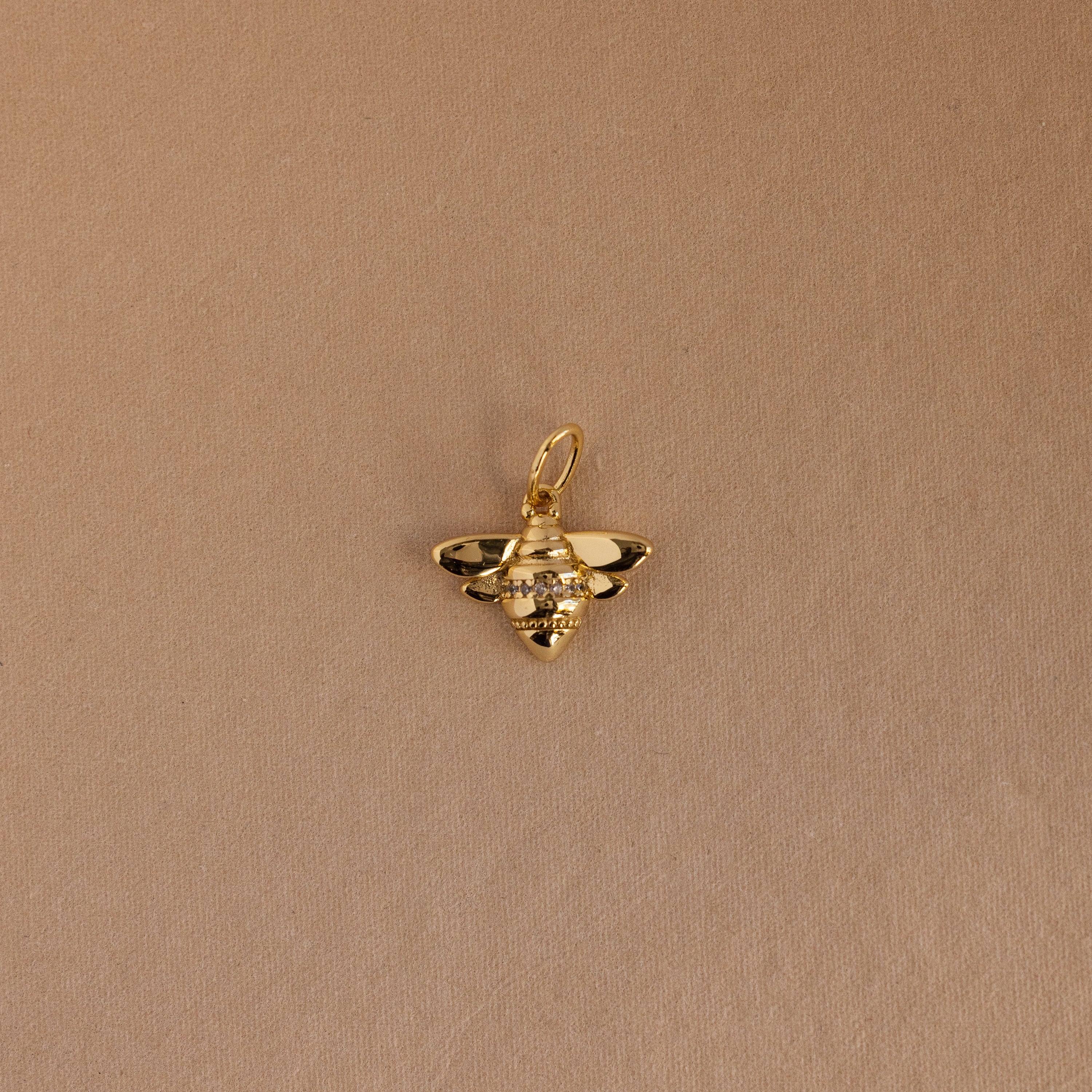 The Honeybee Charm in 18K Gold, adorned with small gemstones, is shown against a plain light brown background.