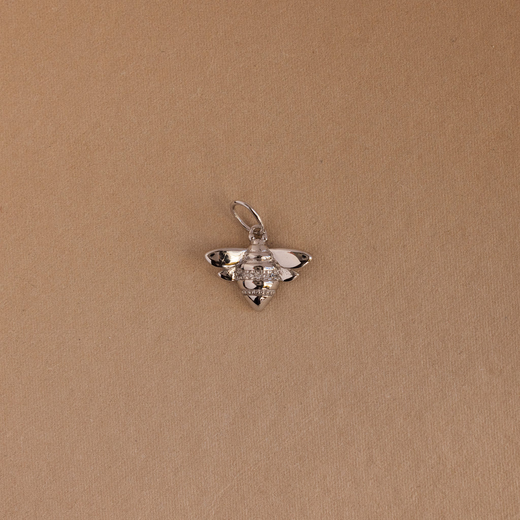 The Honeybee Charm in Sterling Silver, ideal for nature jewelry lovers, is shown on a simple light brown background.