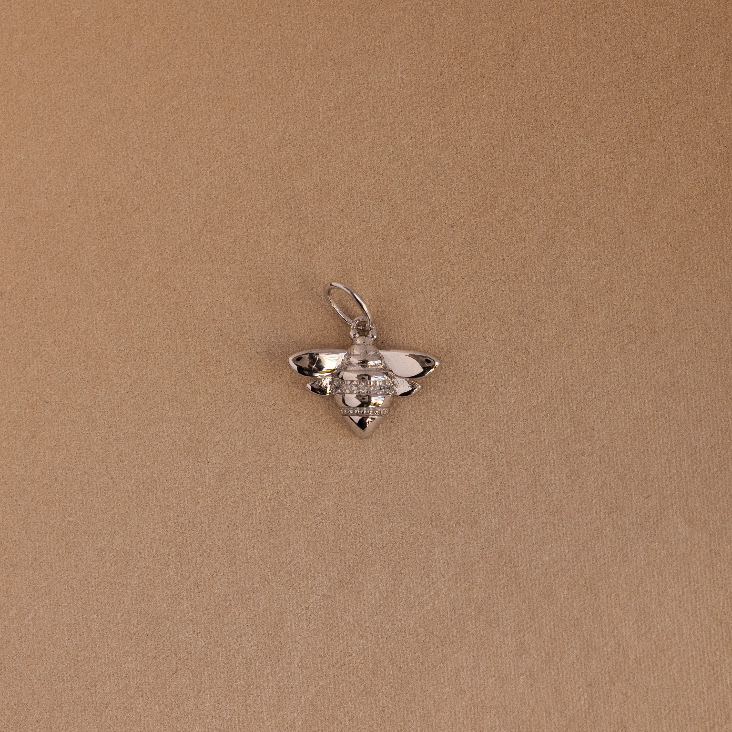 The Honeybee Charm in Sterling Silver, ideal for nature jewelry lovers, is shown on a simple light brown background.