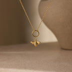 The Honeybee Charm is a delicate gold necklace pendant, inspired by nature and shown against a softly blurred background.