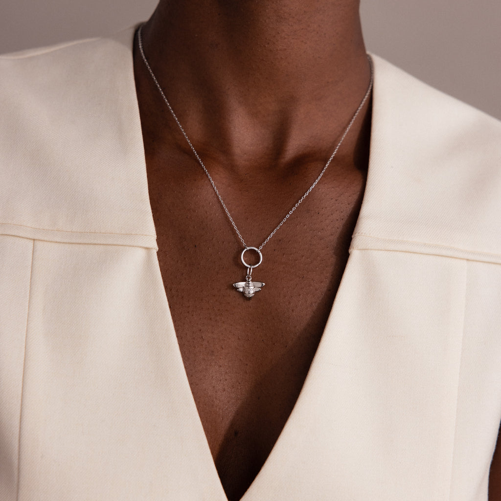 Wearing a cream V-neck top and a Sterling Silver Honeybee Charm necklace, this person embraces the beauty of nature-inspired jewelry.