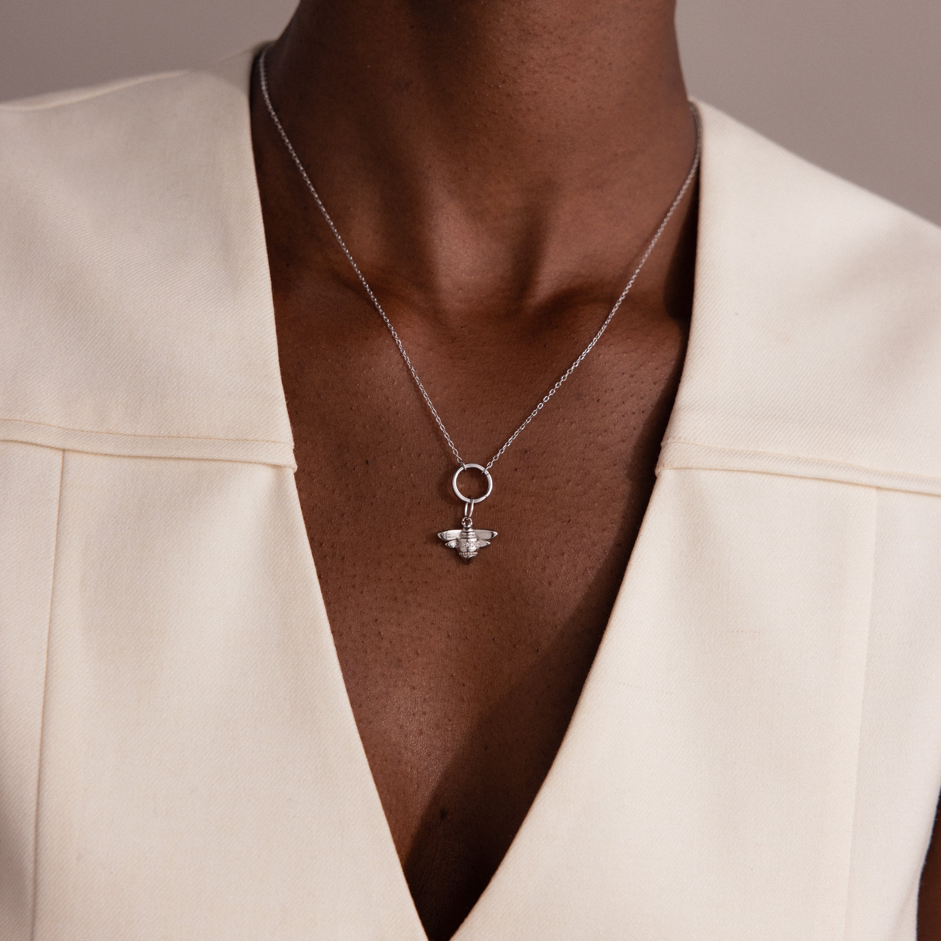 Wearing a cream V-neck top and a Sterling Silver Honeybee Charm necklace, this person embraces the beauty of nature-inspired jewelry.