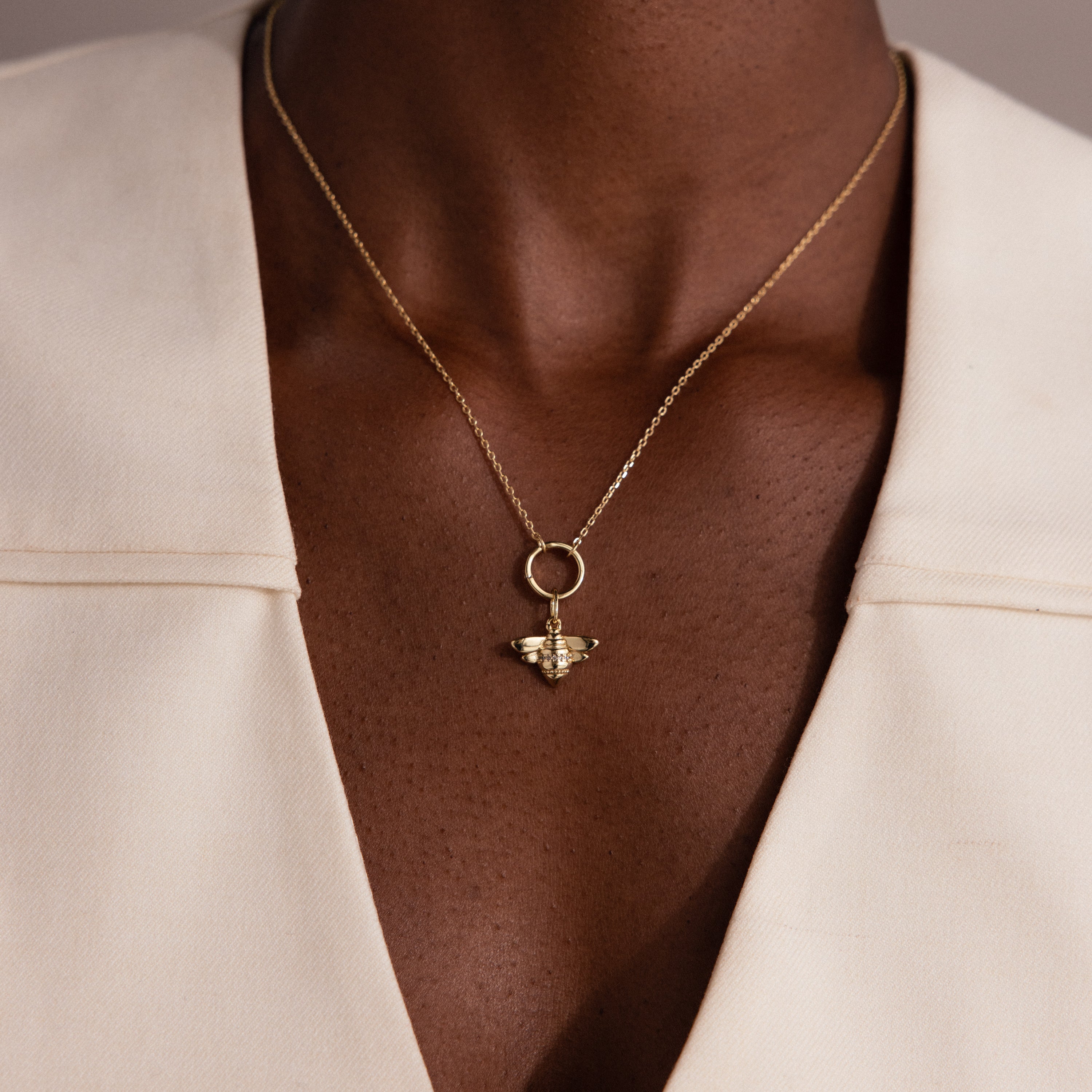 The Honeybee Charm pendant necklace is shown on someone in a cream v-neck, highlighting elegant nature-inspired jewelry.