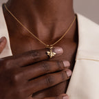 A hand touches the Honeybee Charm in 18K Gold necklace, elegantly worn over a cream-colored blazer.