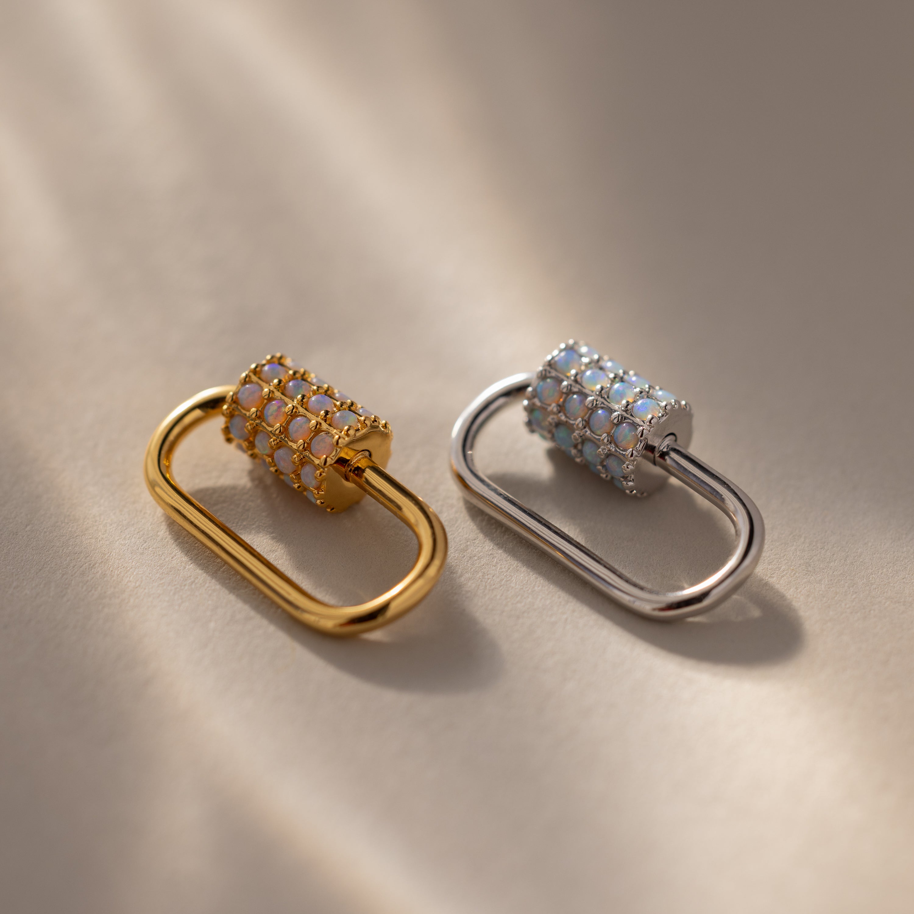 Padlock-shaped gold and silver earrings featuring the Opal Carabiner Clasp and gemstone accents, displayed on a neutral background with soft lighting.