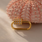 An Opal Carabiner Clasp in 18K Gold rests elegantly on a textured pink sea urchin shell.