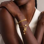 A woman in a white sleeveless top crosses her arms, wearing gold bracelets including one featuring the Opal Carabiner Clasp in 18K Gold.