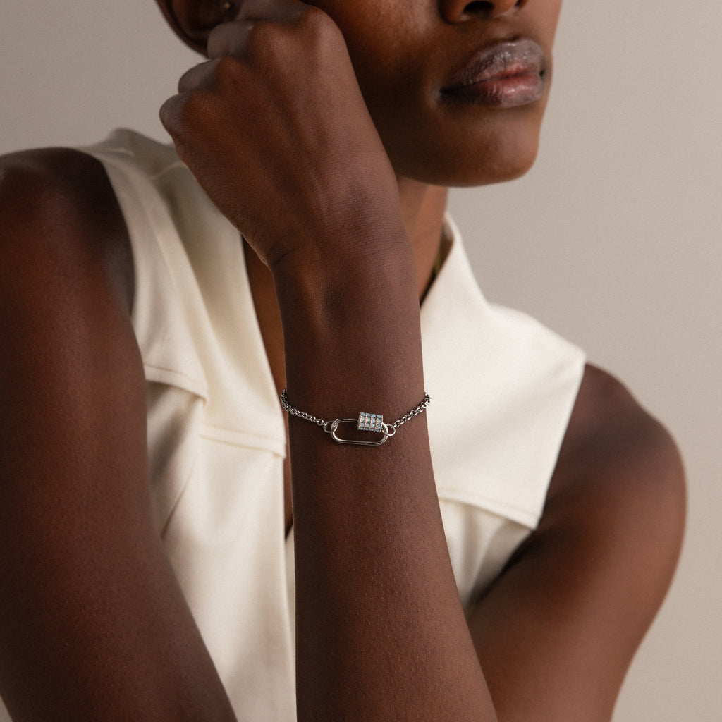 Woman wearing a sleeveless white top and a silver Opal Carabiner Clasp in white gold as a bracelet with a rectangular charm connector detail.