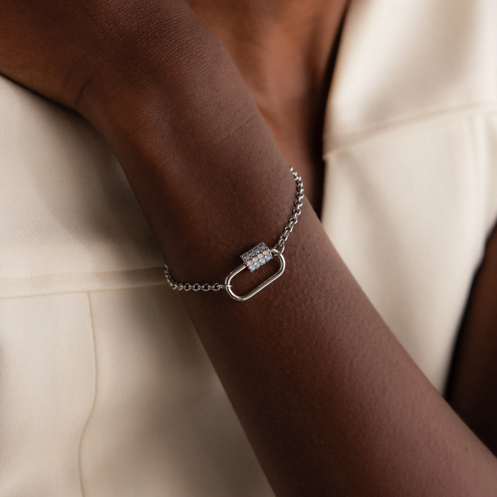 A person wears the Opal Carabiner Clasp in White Gold—a geometric, gem-adorned silver bracelet—paired with a cream outfit.