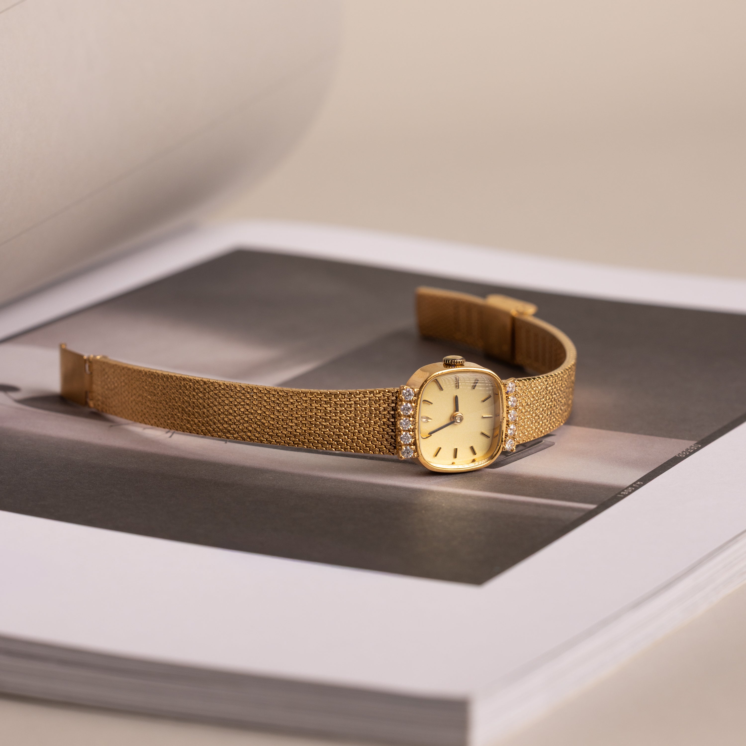 Flatlay image of our Luxe Square Timepiece watch in 18K Gold, laid on a black a white photo