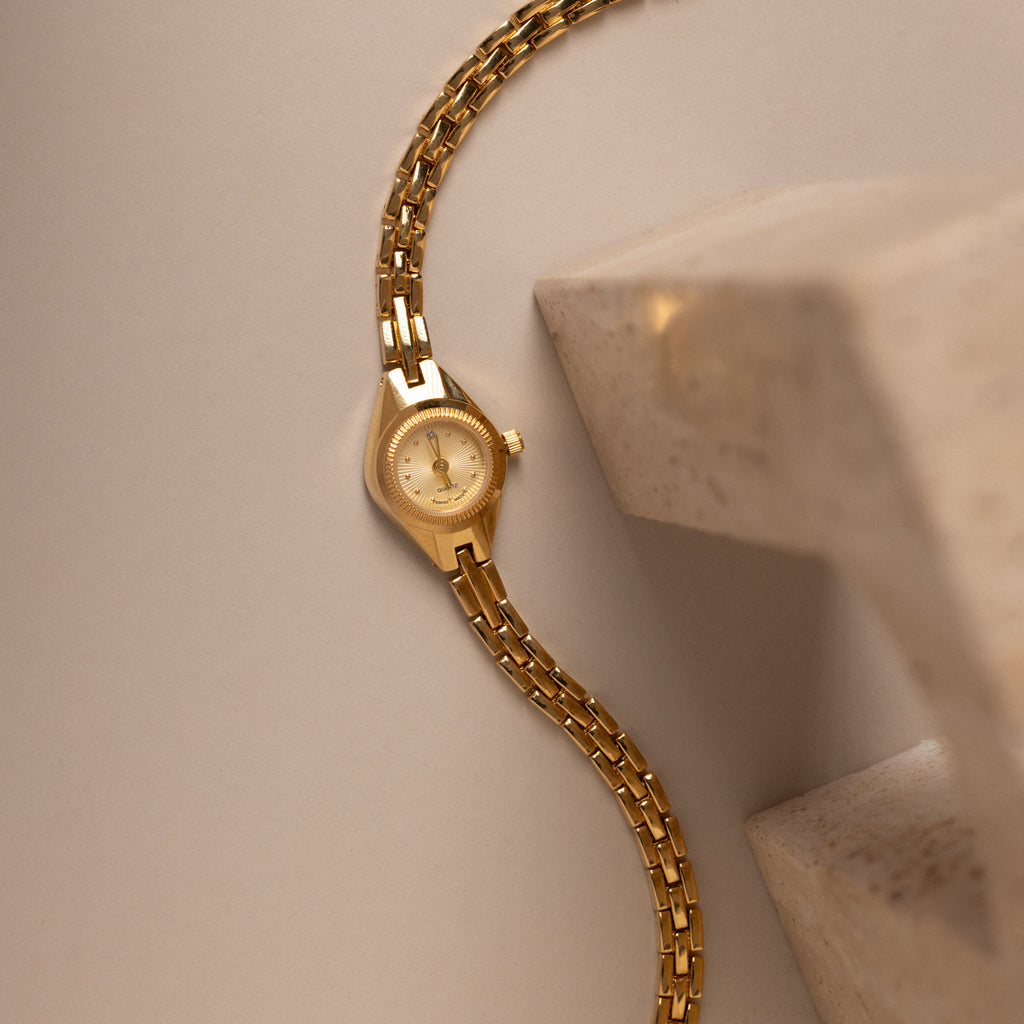 Our Petite Round Timepiece watch on a beige background