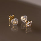 Heart & Flower Earring Backs secure your gold stud earrings with small white pearls—your earring essentials—shown on a reflective brown surface.