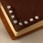 Small transparent heart-shaped objects, similar to Heart & Flower Earring Backs in Sterling Silver, are arranged on a brown suede book—perfect sterling silver earring essentials for your jewelry collection.