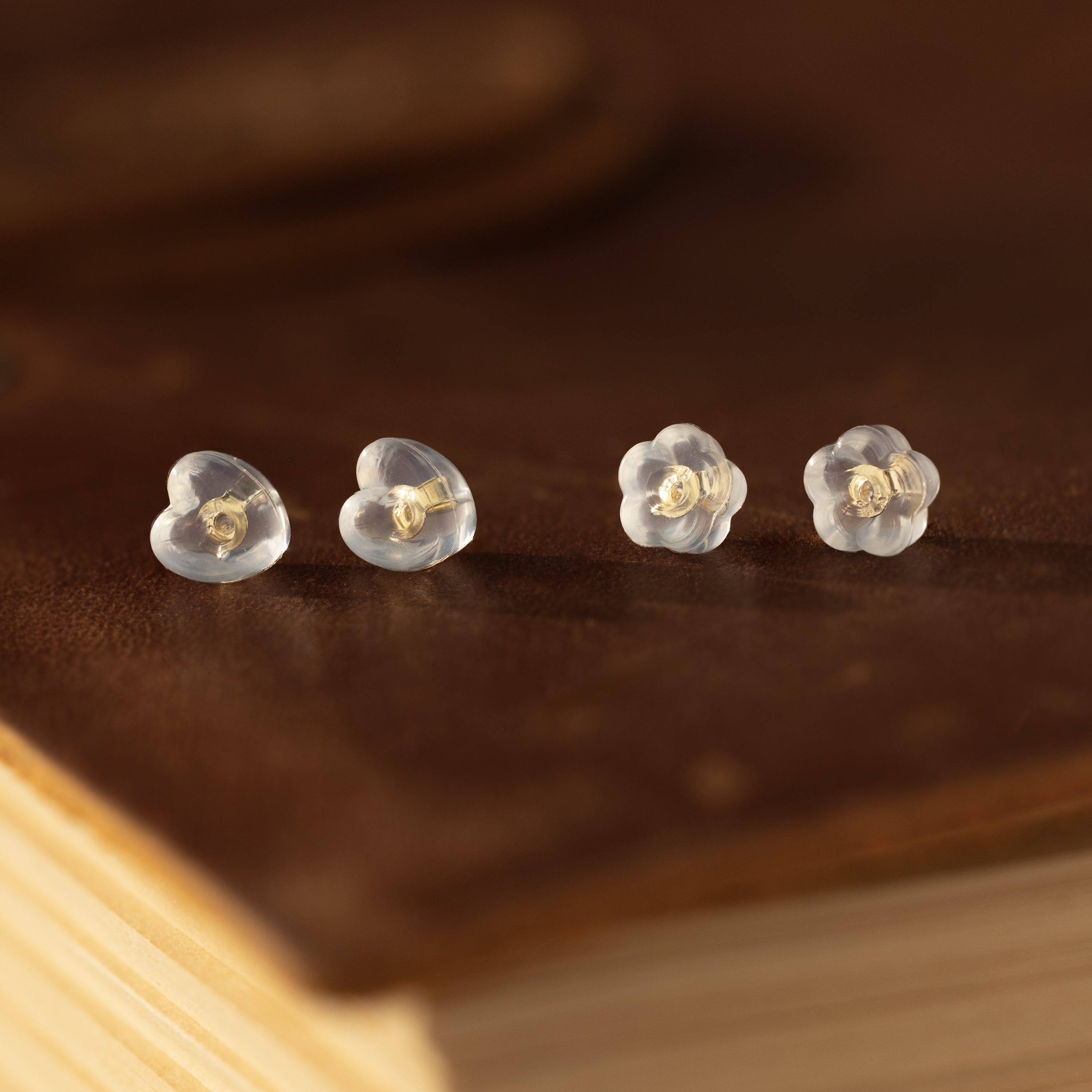 Two pairs of earring essentials: Heart & Flower Earring Backs in 18K Gold, displayed on a brown surface.