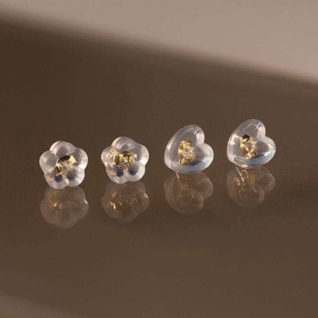 Four Heart & Flower Earring Backs with gold centers, shown on a reflective brown surface—stylish silicone stud backs for secure wear.