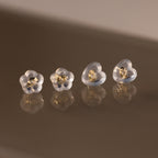 Four Heart & Flower Earring Backs with gold centers, shown on a reflective brown surface—stylish silicone stud backs for secure wear.