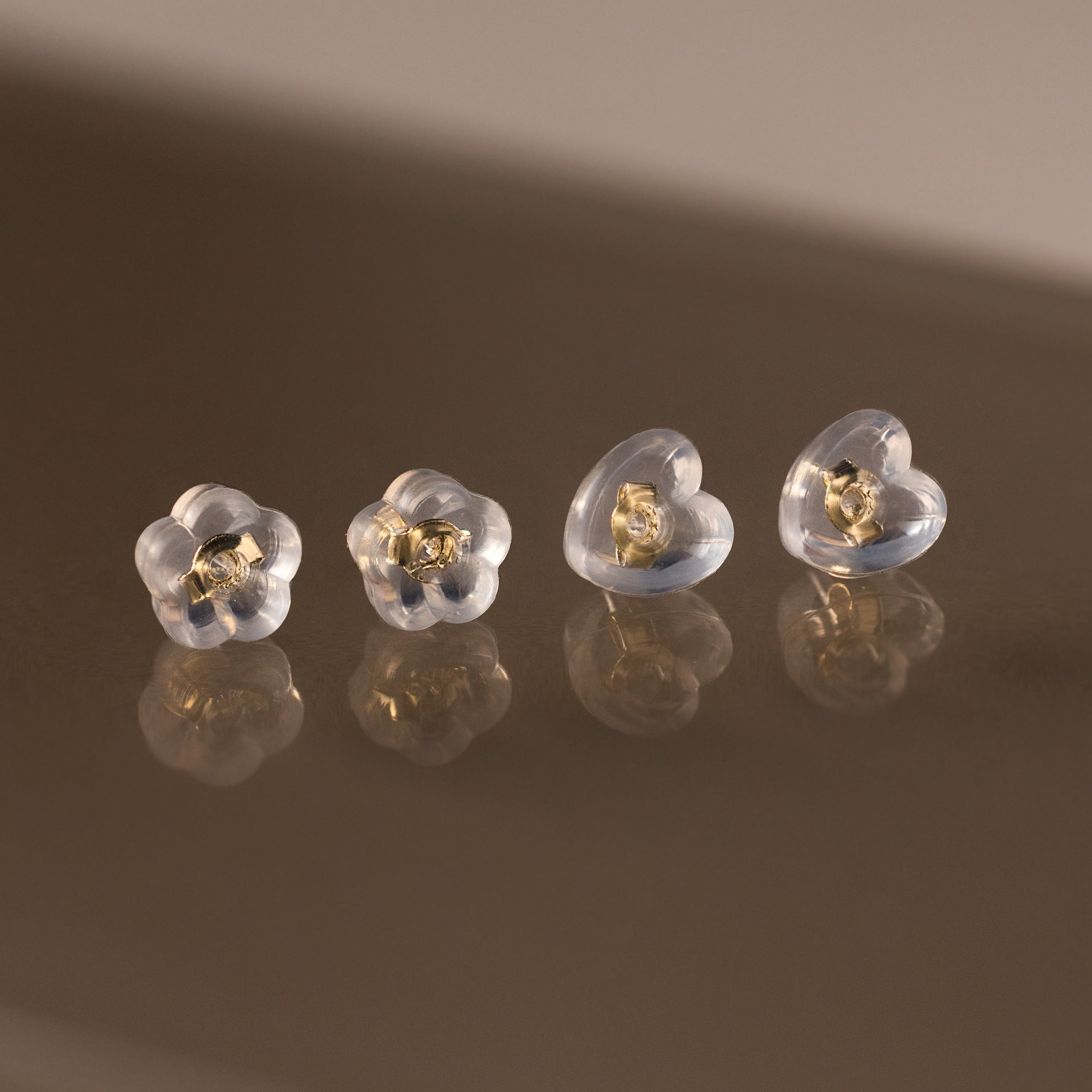 Four Heart & Flower Earring Backs with gold centers, shown on a reflective brown surface—stylish silicone stud backs for secure wear.