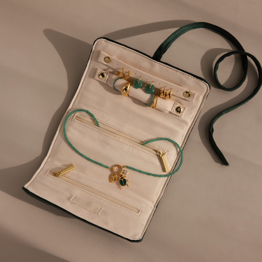 The Velvet Roll-Up Jewelry Case is shown on a beige background with gold earrings, a green beaded necklace, and gold charms.