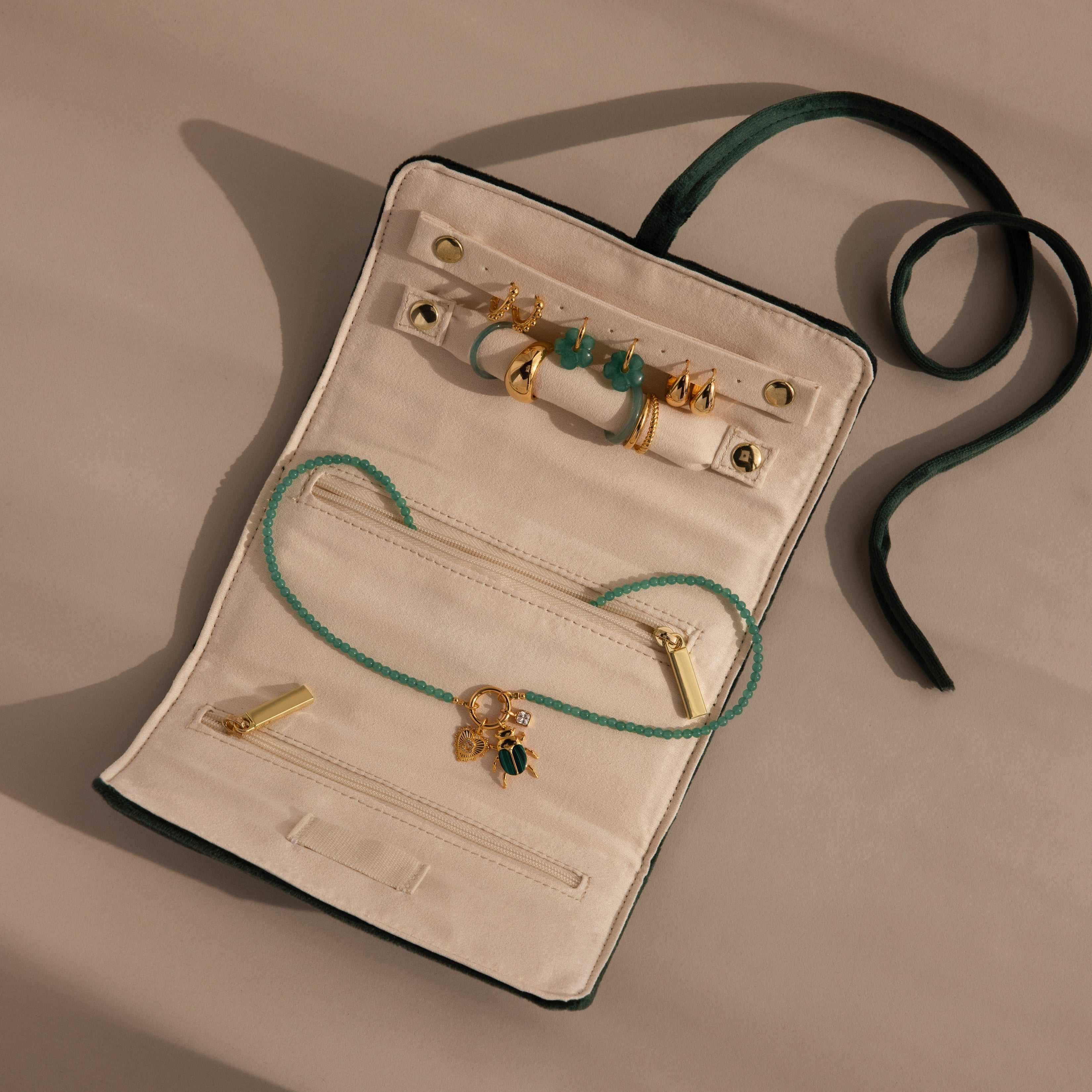 The Velvet Roll-Up Jewelry Case is shown on a beige background with gold earrings, a green beaded necklace, and gold charms.