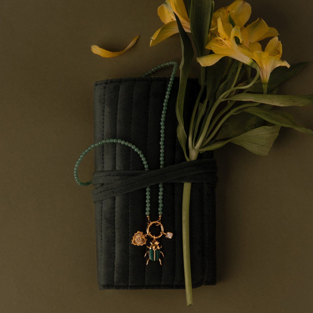 A green beaded necklace and yellow flowers are displayed on a Velvet Roll-Up Jewelry Case with an olive background.