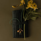 A green beaded necklace and yellow flowers are displayed on a Velvet Roll-Up Jewelry Case with an olive background.