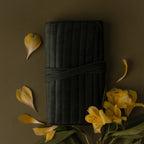 A Velvet Roll-Up Jewelry Case, surrounded by yellow flowers and petals, is displayed on an olive green background.