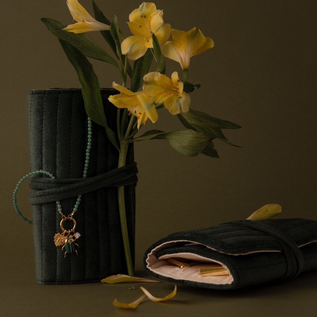 Two dark green Velvet Roll-Up Jewelry Cases with yellow flowers and jewelry, displayed on an olive background—ideal as stylish travel organizers.