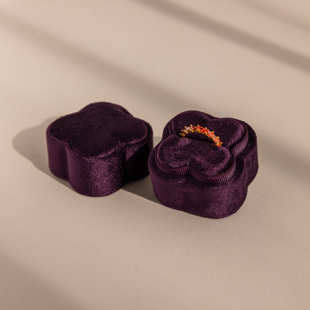 The Purple Flower Velvet Ring Box, ideal for proposals, is shaped like a flower and holds a sparkling ring inside as it sits on a beige surface.