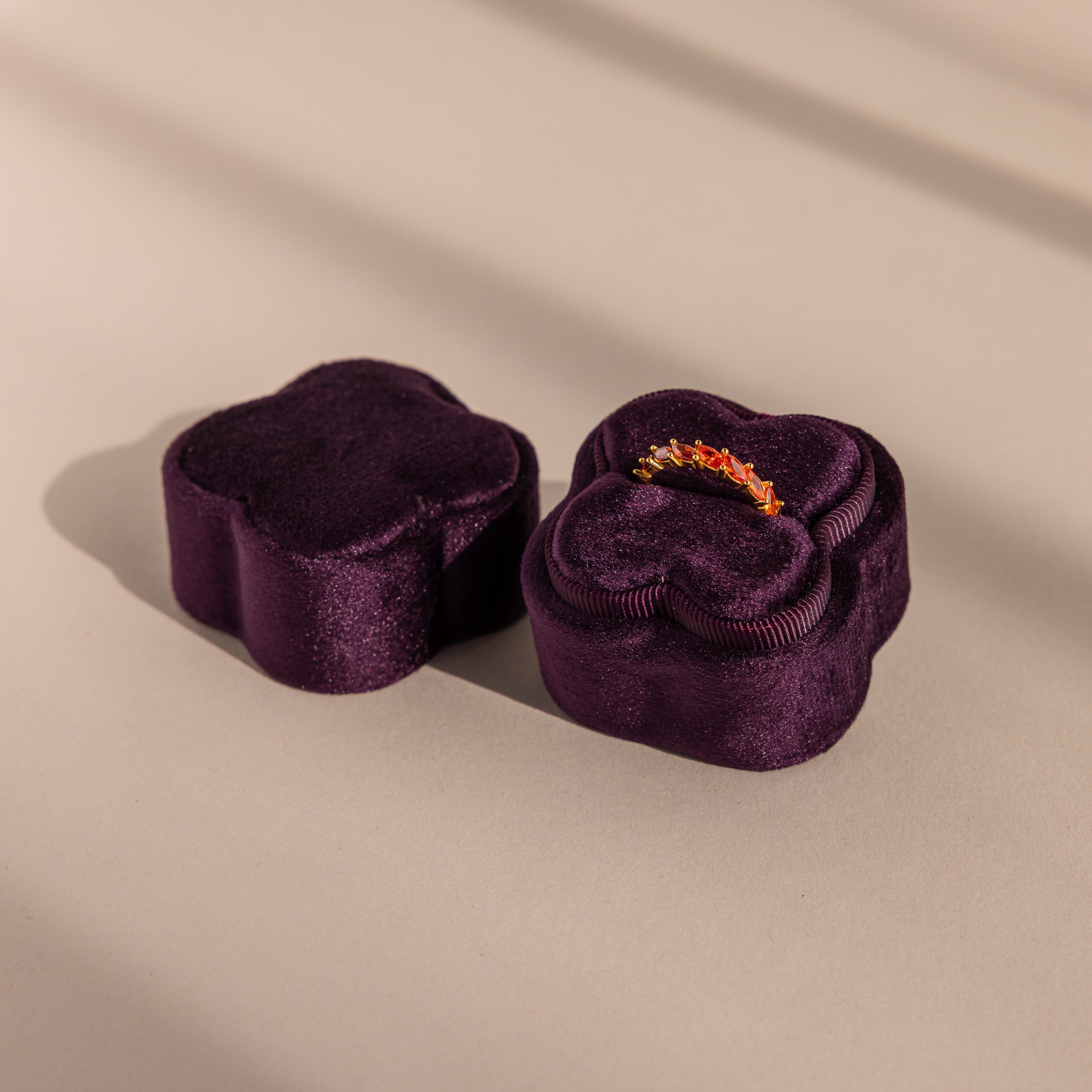 The Purple Flower Velvet Ring Box, ideal for proposals, is shaped like a flower and holds a sparkling ring inside as it sits on a beige surface.