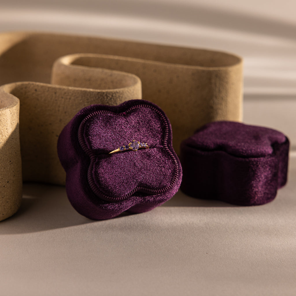 Gold ring with small diamonds in the Purple Flower Velvet Ring Box, featuring a matching purple lid and neutral background decor.