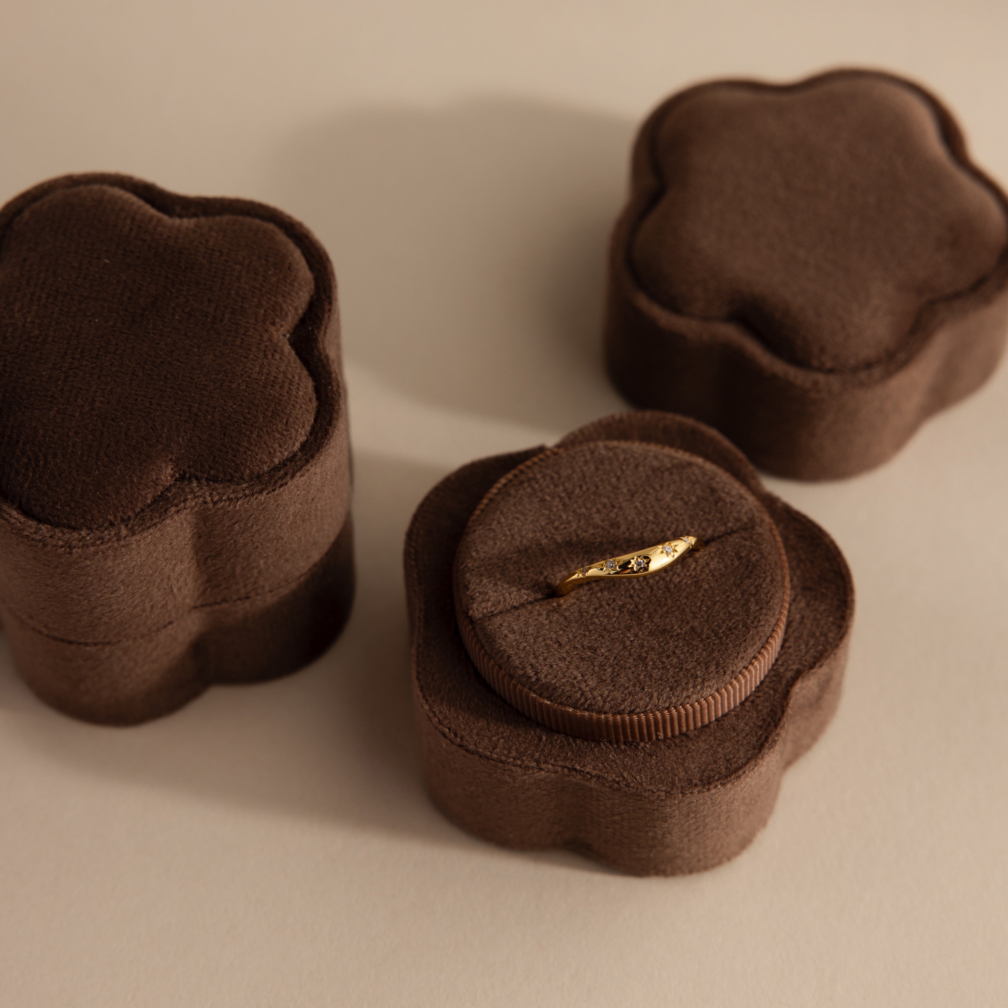A gold ring displayed in the Brown Flower Velvet Ring Box, with two similar closed boxes beside it.