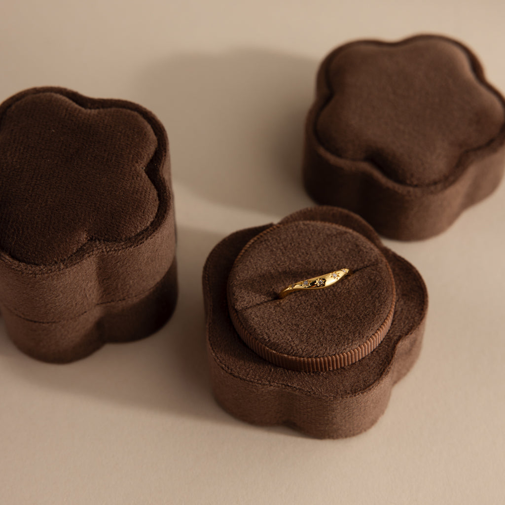 A gold ring sits in a Flower Velvet Ring Box—brown and flower-shaped—with two similar boxes beside it on a light surface.
