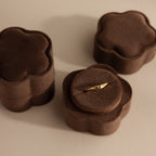 A gold ring sits in a Flower Velvet Ring Box—brown and flower-shaped—with two similar boxes beside it on a light surface.
