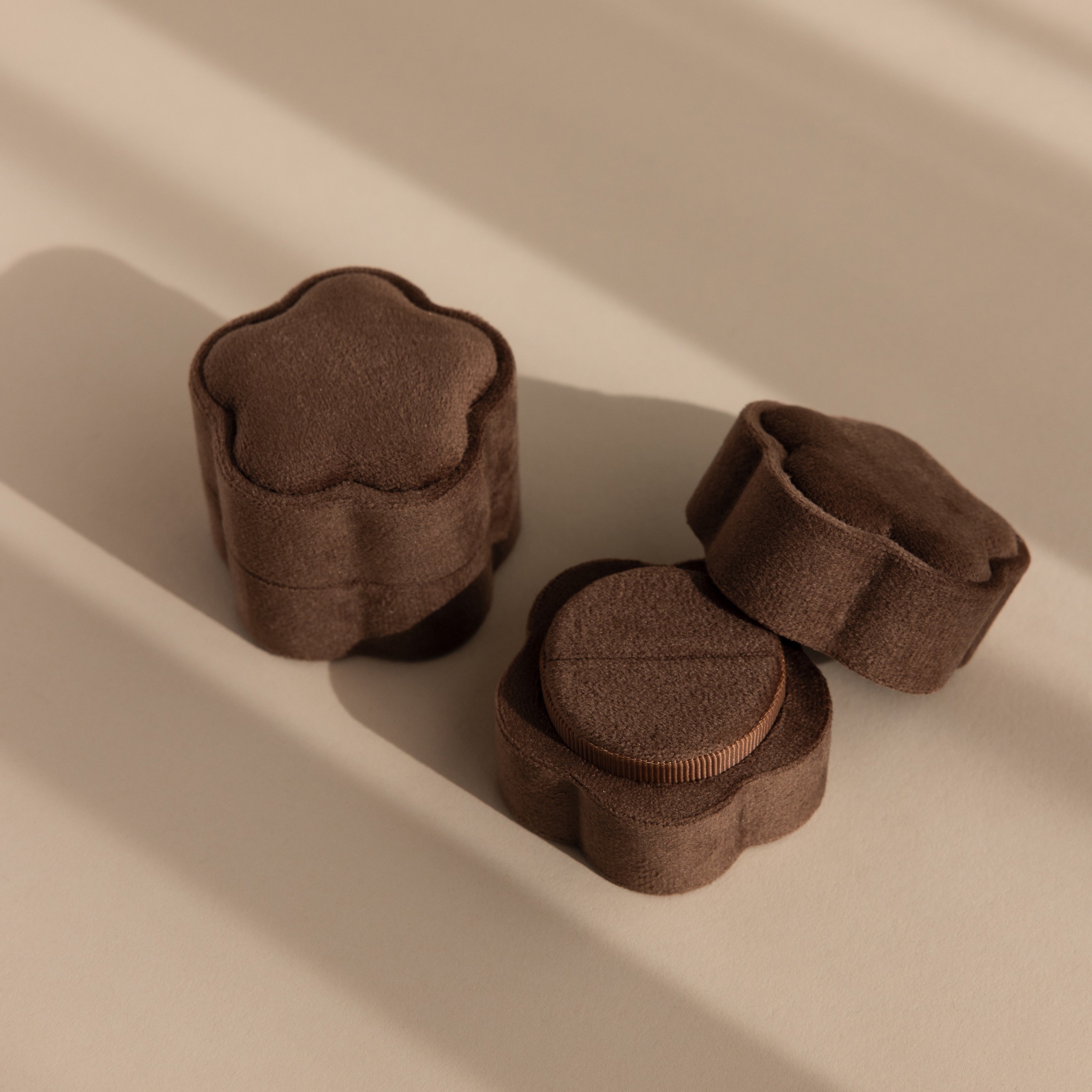 Three Brown Flower Velvet Ring Boxes sit on a beige surface with soft shadows—perfect for treasuring your special proposal moments. Try the Brown Flower Velvet Ring Box for an elegant touch.