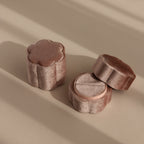 Two Flower Velvet Ring Boxes in pink velvet, shaped like flowers, rest on a beige surface and cast soft shadows.