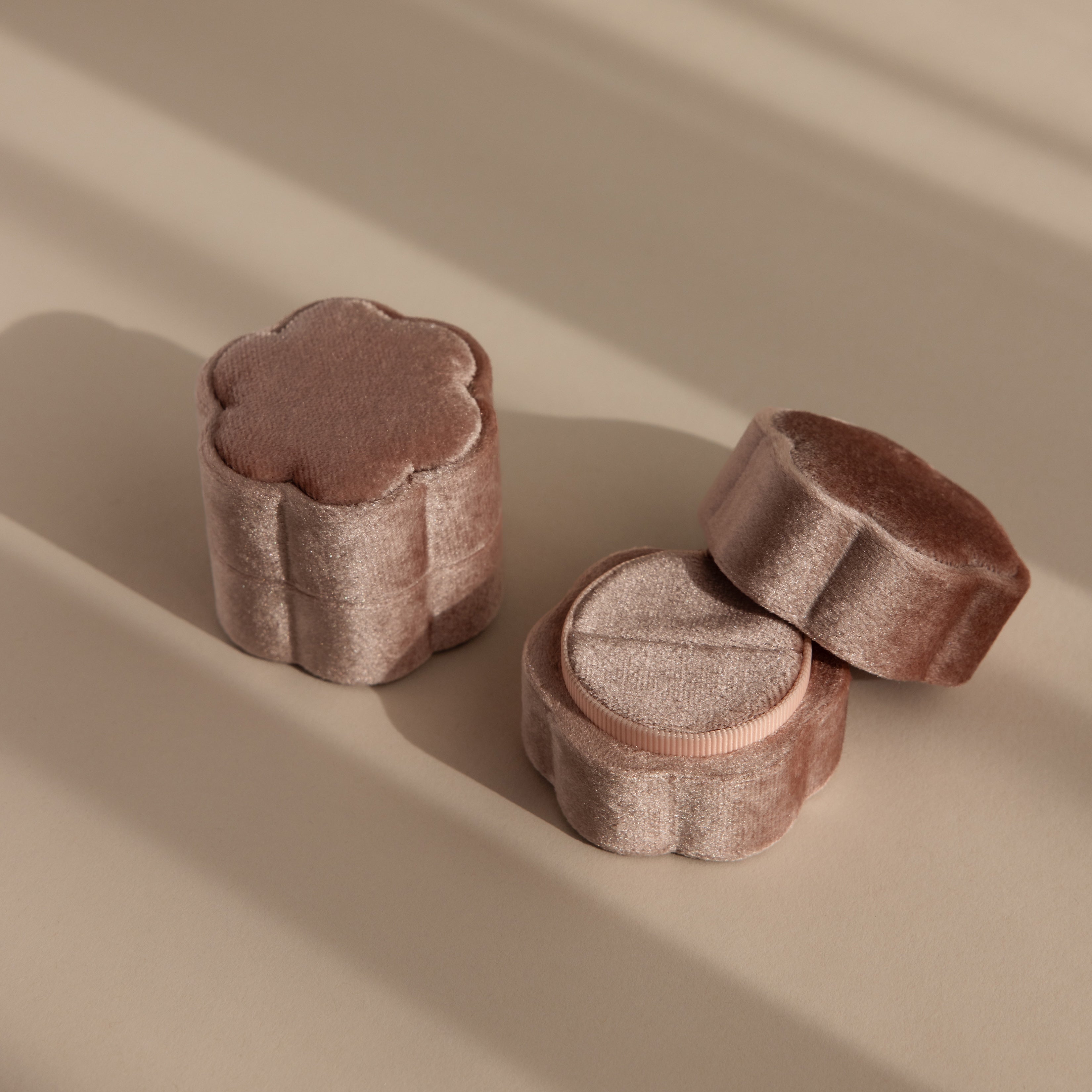 Two Flower Velvet Ring Boxes in pink velvet, shaped like flowers, rest on a beige surface and cast soft shadows.