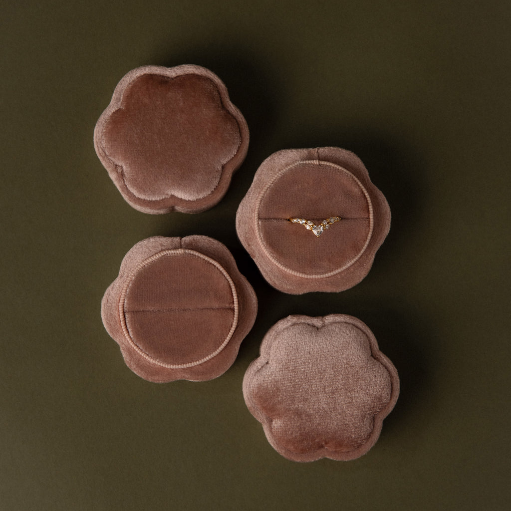 Four Pink Flower Velvet Ring Boxes, one open to reveal a delicate diamond ring, arranged on an olive background.
