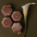 Four Flower Velvet Ring Boxes in pink, ideal for proposals, displayed with gold rings beside a white calla lily on an olive green background.