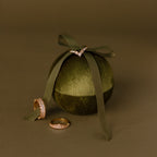 Three gold rings are displayed on and next to the Green Velvet Round Ring Box, which is elegantly tied with a matching ribbon.