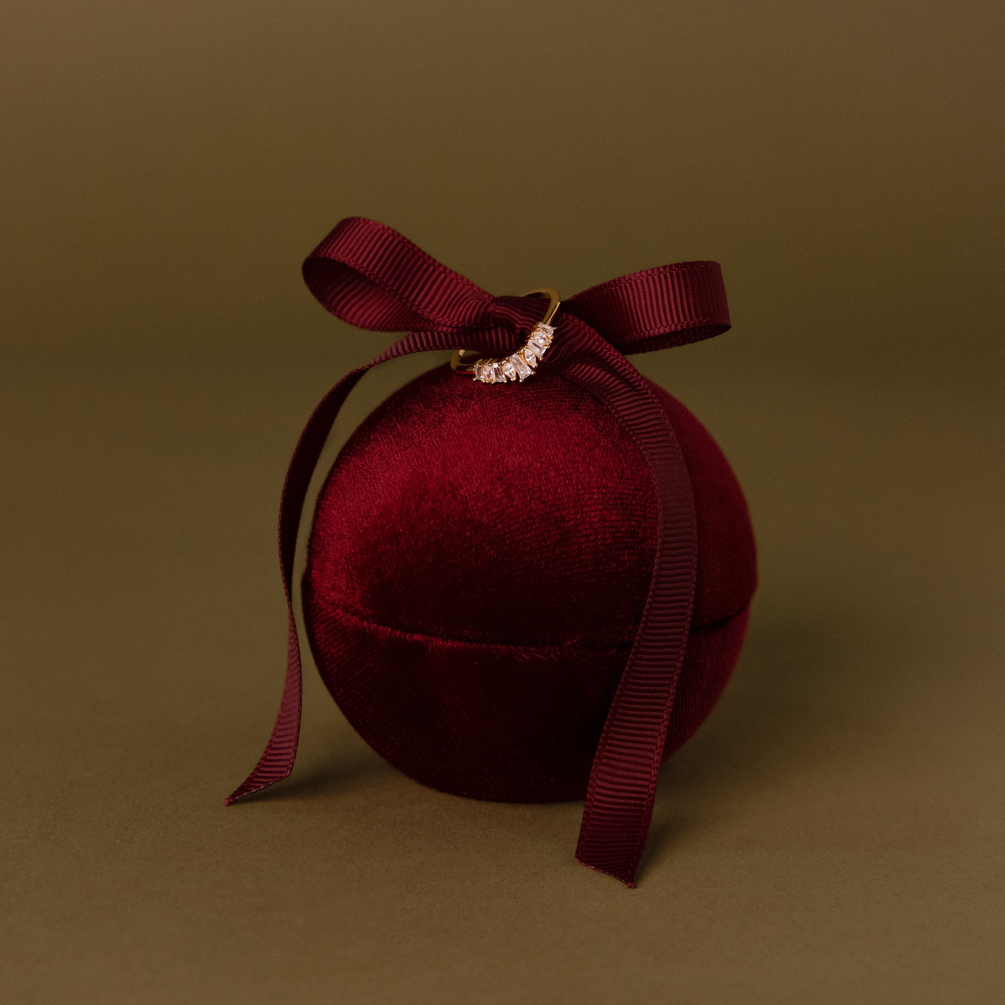A Red Velvet Round Ring Box with a matching ribbon bow, beautifully displayed against a brown background—an elegant choice for presenting your special ring on any occasion.