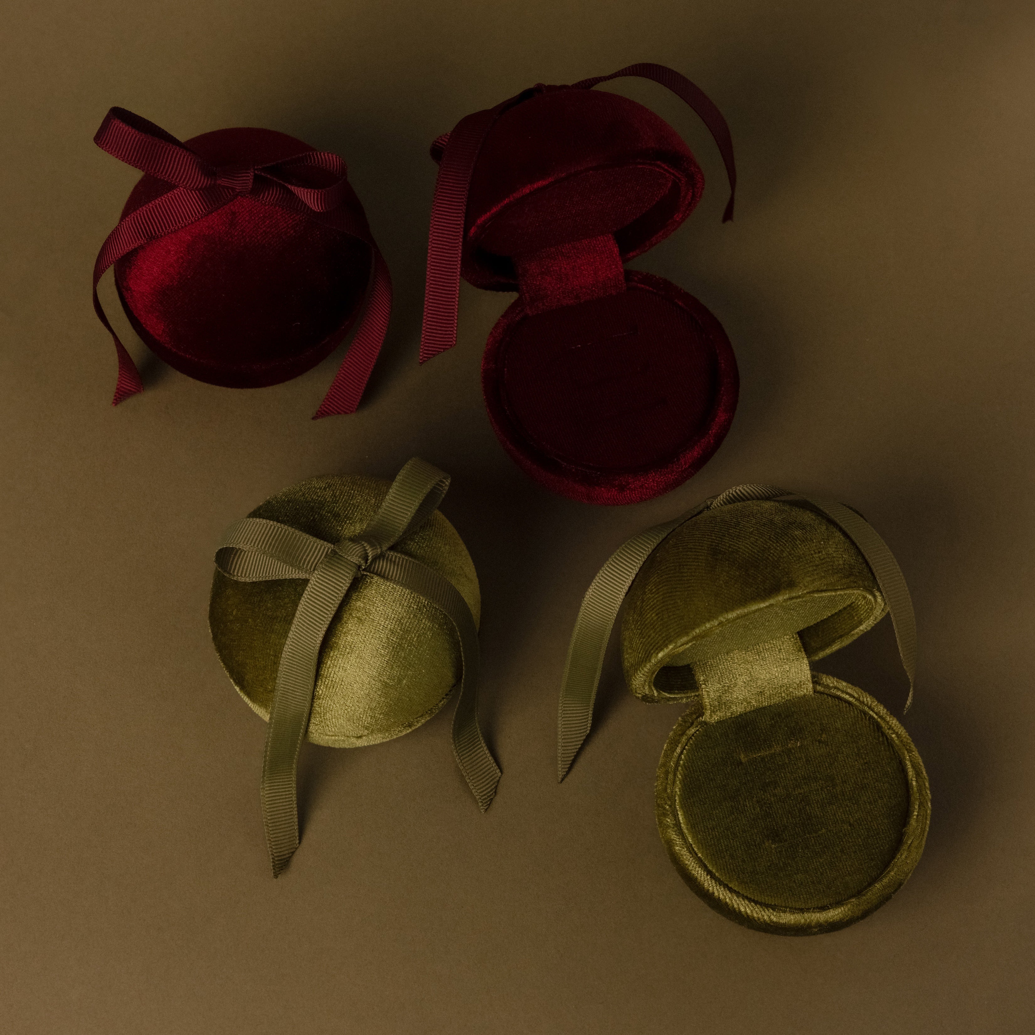Four Velvet Round Ring Boxes—two red, two green—with ribbon closures are arranged on a brown surface, each serving as an elegant Velvet Round Ring Box for presenting your rings.