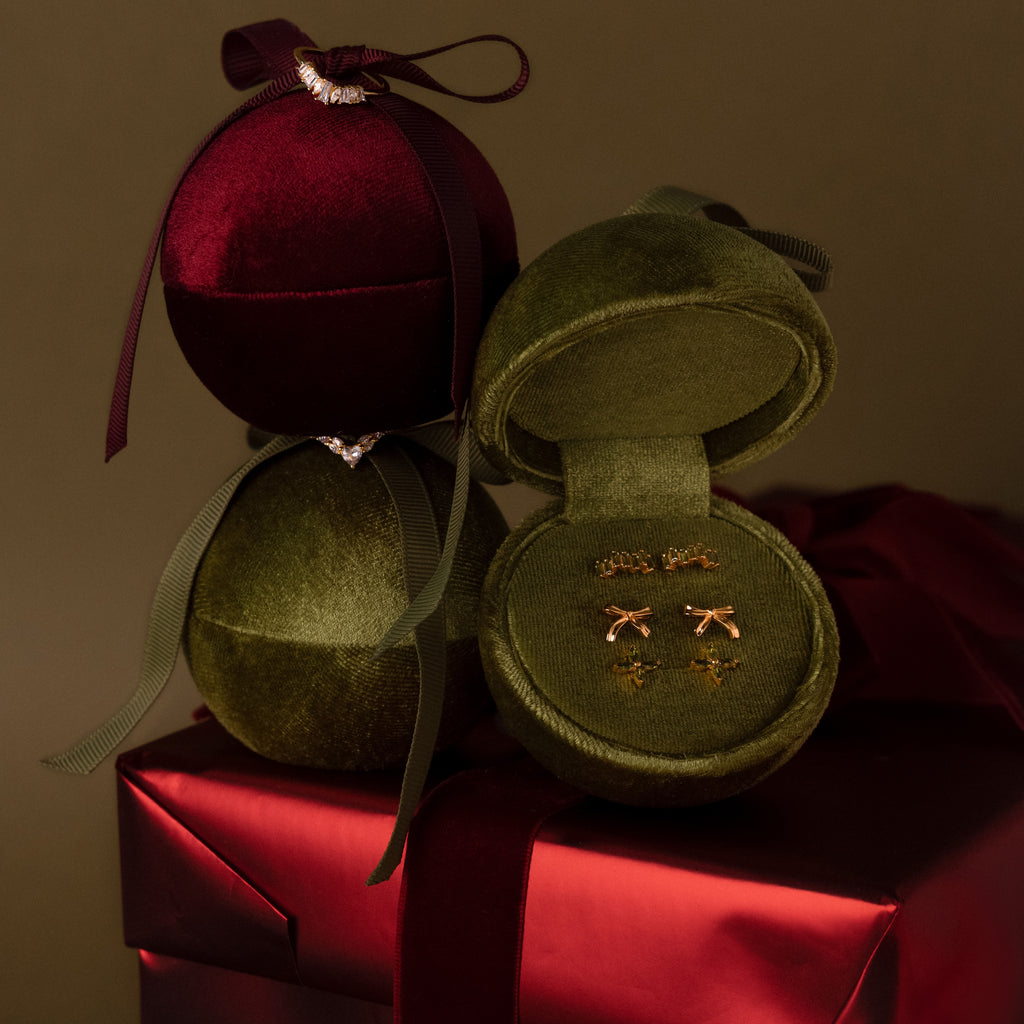 A Green Velvet Round Ring Box, opened to showcase gold earrings, sits on a red gift box with ribbon—an elegant jewelry display ideal for gifting.