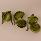 Three Green Velvet Round Ring Boxes—two open, one closed with ribbons; one box displays a pair of earrings.