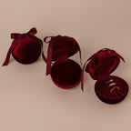 Three Red Velvet Round Ring Boxes—one closed, two open showcasing gold rings—serve as elegant ring holders on a beige background.