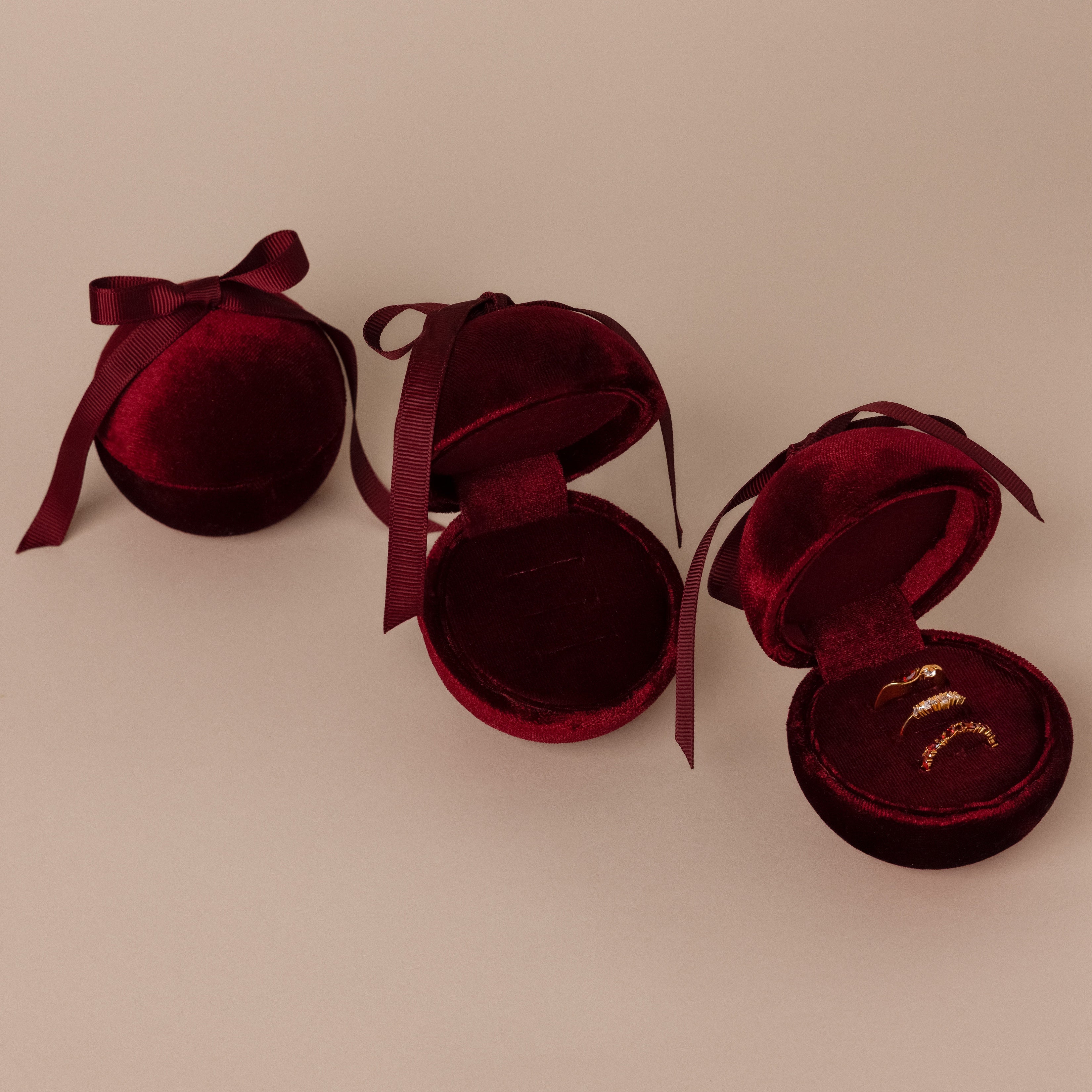 Three Red Velvet Round Ring Boxes—one closed, two open showcasing gold rings—serve as elegant ring holders on a beige background.