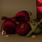 Three gold rings displayed in a Red Velvet Round Ring Box, with additional rings and ribbon-wrapped boxes nearby.