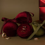 The Velvet Round Ring Box with ribbon bow holds gold rings and is displayed on a neutral background alongside a red jewelry gift box.