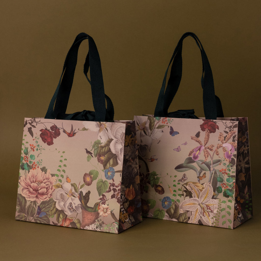 The Gift Wrap Add-On features two floral-patterned gift bags with dark handles, offering an elegant wrapping solution, shown on a plain olive-green background.