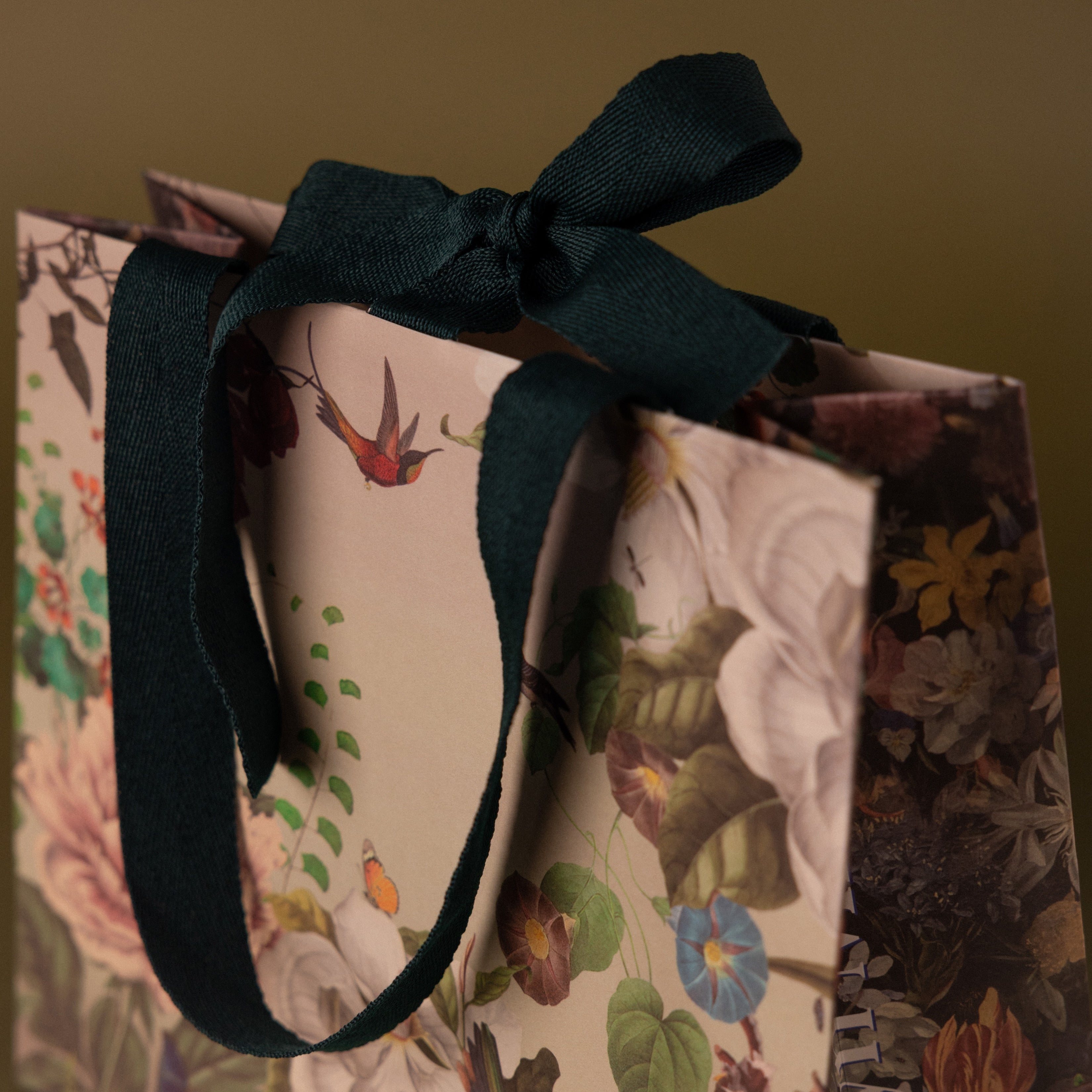 Gift Wrap Add-On: Floral gift bag with dark green ribbon handles and bow, adorned with vibrant botanical illustrations—an elegant finishing touch for your gift wrapping.